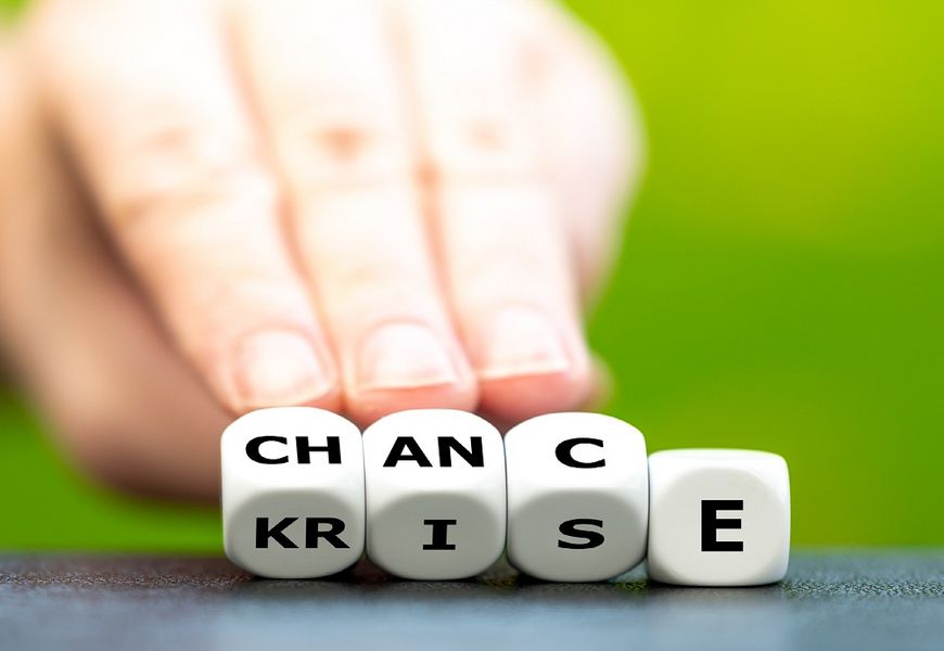 Eine Hand wendet Würfel mit Buchstaben von dem Wort "Krise" hin zu dem Wort "Chance".